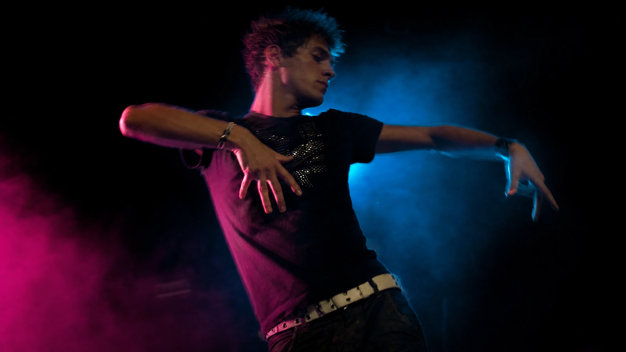 AI dancer performing a sharp arm wave under magenta and cyan stage light